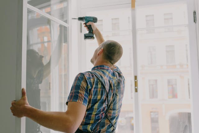 man drilling into an open window frame