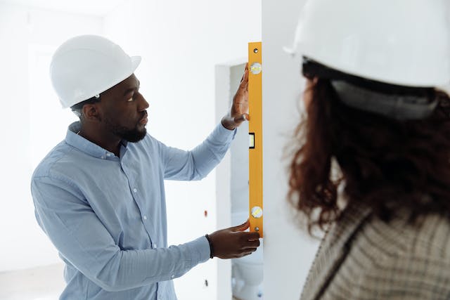 two people in hardhats using a level to measure a wall
